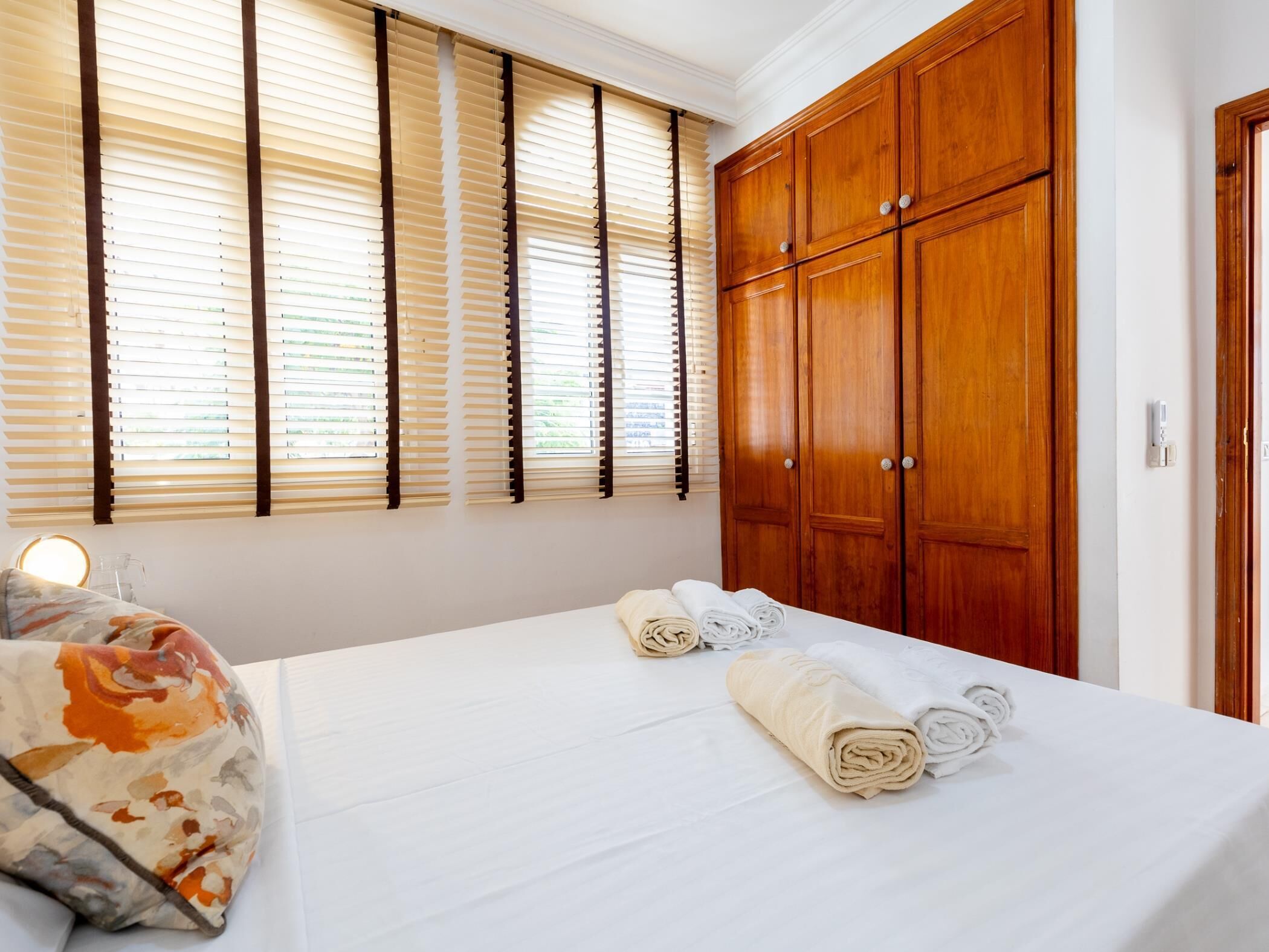 Une chambre d’hôtel avec un lit, une armoire en bois et une fenêtre avec des stores.
