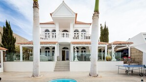 Ein großes, weißes Gebäude mit einem Ziegeldach, einem Swimmingpool und Palmen.