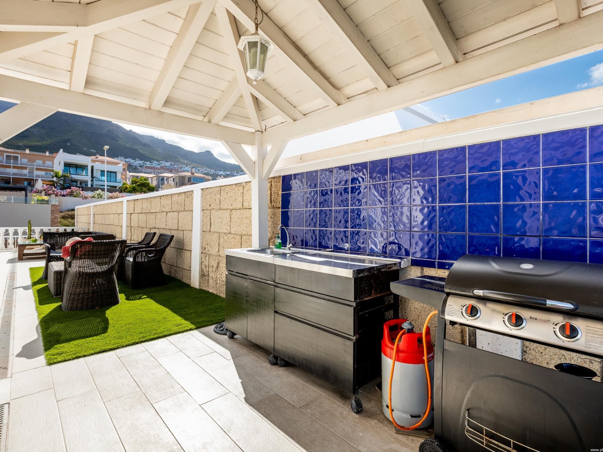 An outdoor kitchen area with a grill, sink, and seating area with chairs and a table.
