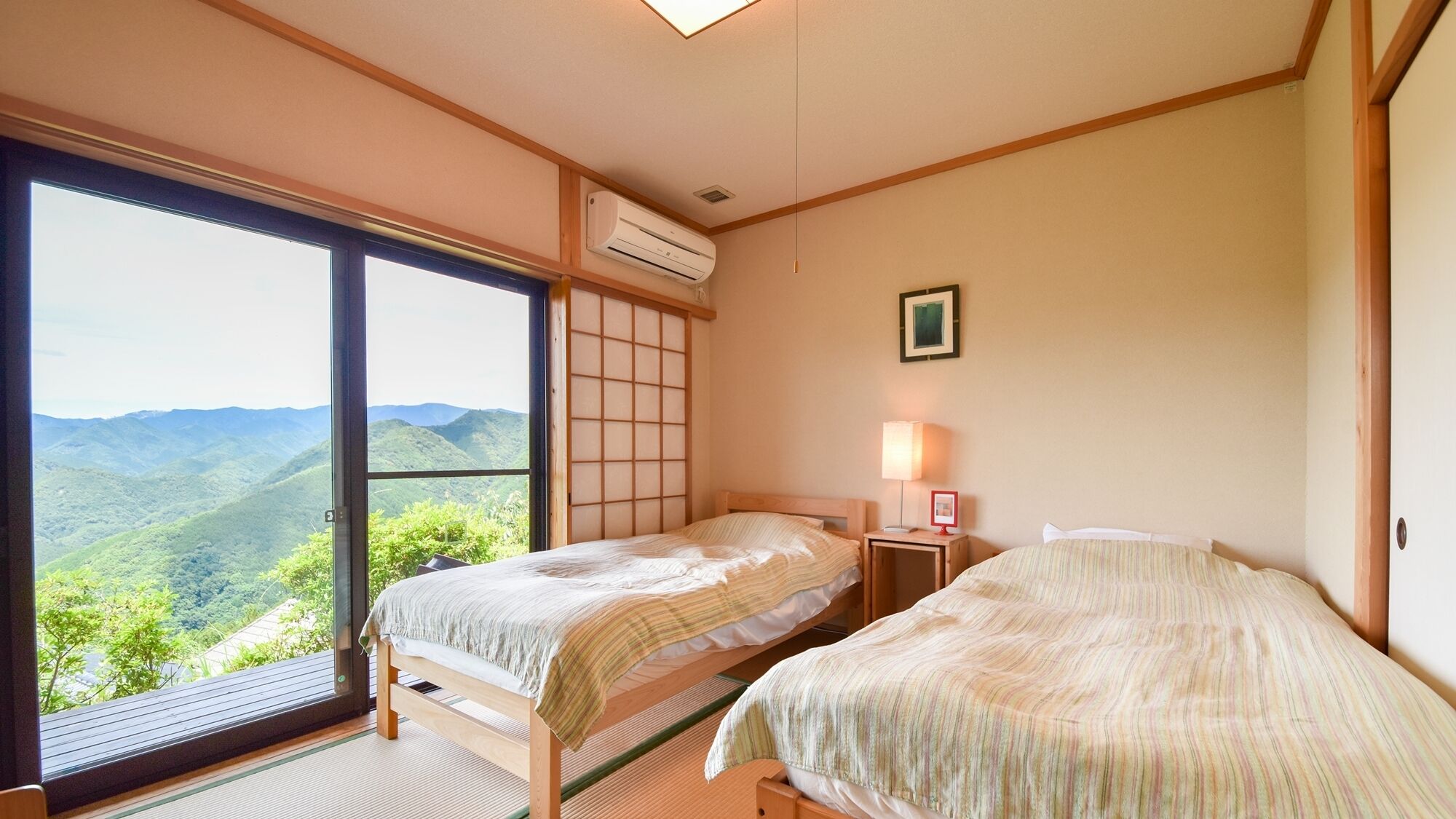 Ein Schlafzimmer mit zwei Betten, einem verschiebbaren Shoji-Bildschirm, einer Klimaanlage und Blick auf eine gebirgige Landschaft.