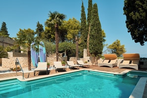 Relax by the serene pool surrounded by lush trees and lounge chairs.