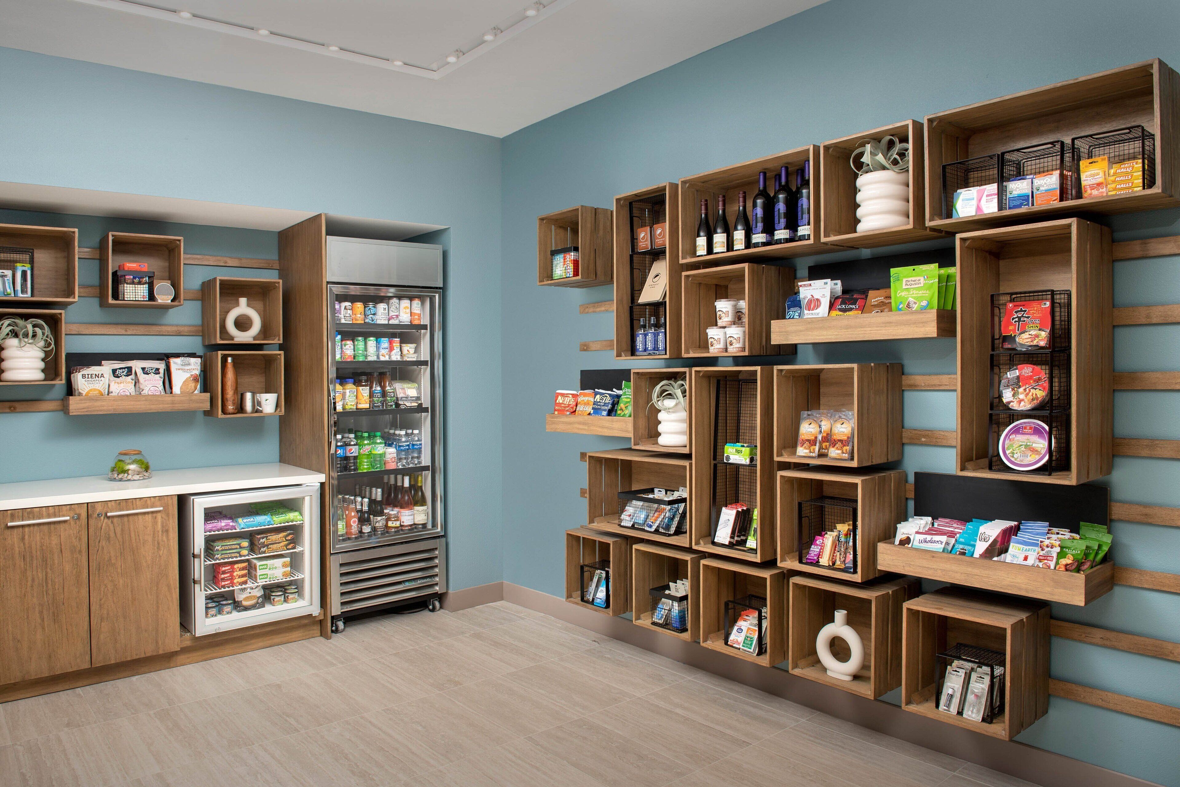 Un espace de vente bien aménagé, avec des étagères en bois où sont exposés divers produits, un présentoir réfrigéré et un petit comptoir équipé d’un réfrigérateur.