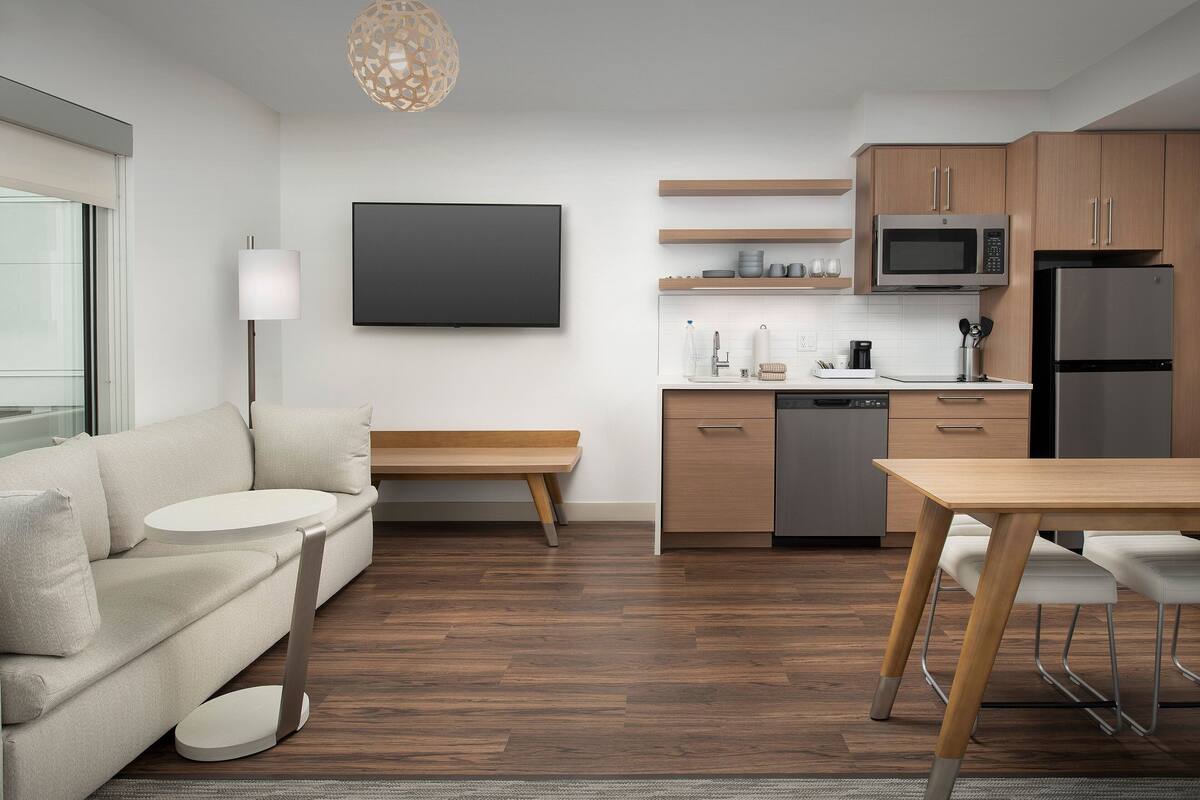 A modern kitchen with wooden cabinets, a microwave, a refrigerator, and a dining area with a table and chairs.