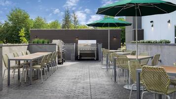 An outdoor patio with brick flooring, wicker chairs, and tables, a grill, and green umbrellas.