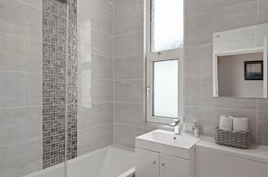 Ein modernes Badezimmer mit Duschkabine aus Glas, einem großen Fenster und einem weißen Waschtisch mit Spiegel und Handtuchhalter.