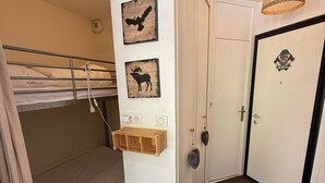 Een slaapkamer met stapelbed, een houten plank, een deur met logo en twee aan de muur hangende foto's.