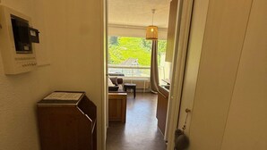 Een gang die uitkomt op een balkon met uitzicht op groen, een radiator en een hanglamp.