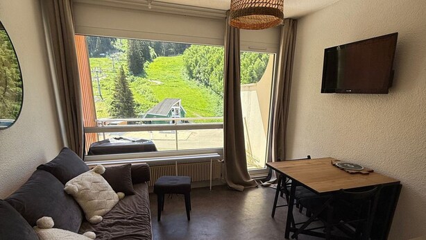 Een gezellige kamer met een bank, een klein tafeltje en een aan de muur bevestigde televisie.