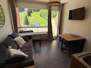 A cozy room with a sofa, a small table, and a TV mounted on the wall. - Studio cabin 24m² at the foot of the slopes with balcony (Les Adrets-Prapoutel)