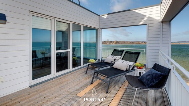 A deck with two lounge chairs, a small table with fruit, and a view of the sea. - Lütthoorn-1st row by the water, wood-burning stove, sauna, roof terrace, barbecu (Olpenitz)
