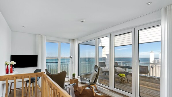 A spacious balcony with a view of the sea, a wooden railing, and a seating area with a table and chairs.