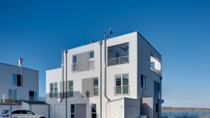 A modern multi-story residential building with a flat roof, large windows, and balconies. - Lütthoorn-1st row by the water, wood-burning stove, sauna, roof terrace, barbecu (Olpenitz)