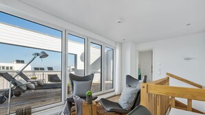 A modern living room with large windows, a wooden staircase, and a view of the cityscape. - Lütthoorn-1st row by the water, wood-burning stove, sauna, roof terrace, barbecu (Olpenitz)