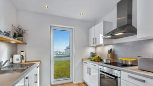 A modern kitchen with white cabinets, stainless steel appliances, a large window, and a view of the city. - Lütthoorn-1st row by the water, wood-burning stove, sauna, roof terrace, barbecu (Olpenitz)