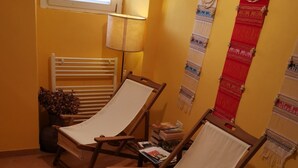 Pieni huone, jossa on kaksi puutuolia, ikkuna, patteri ja kaksi seinälle ripustettua koristetta.