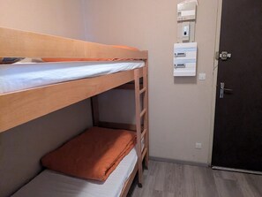 Quarto com beliche, escada de madeira, porta e tomadas na parede.