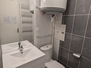 Casa de banho com lavatório branco, sanita e uma prateleira de vidro sobre a sanita.