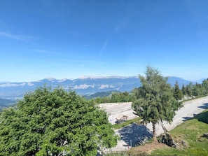 Ein Gebirgssträßchen mit freiem Blick auf ferne Berge und ein Parkplatz mit Unterstand.