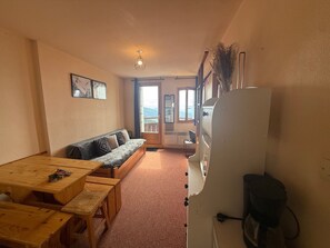 A compact room with a wooden table, benches, a sofa, and a refrigerator.