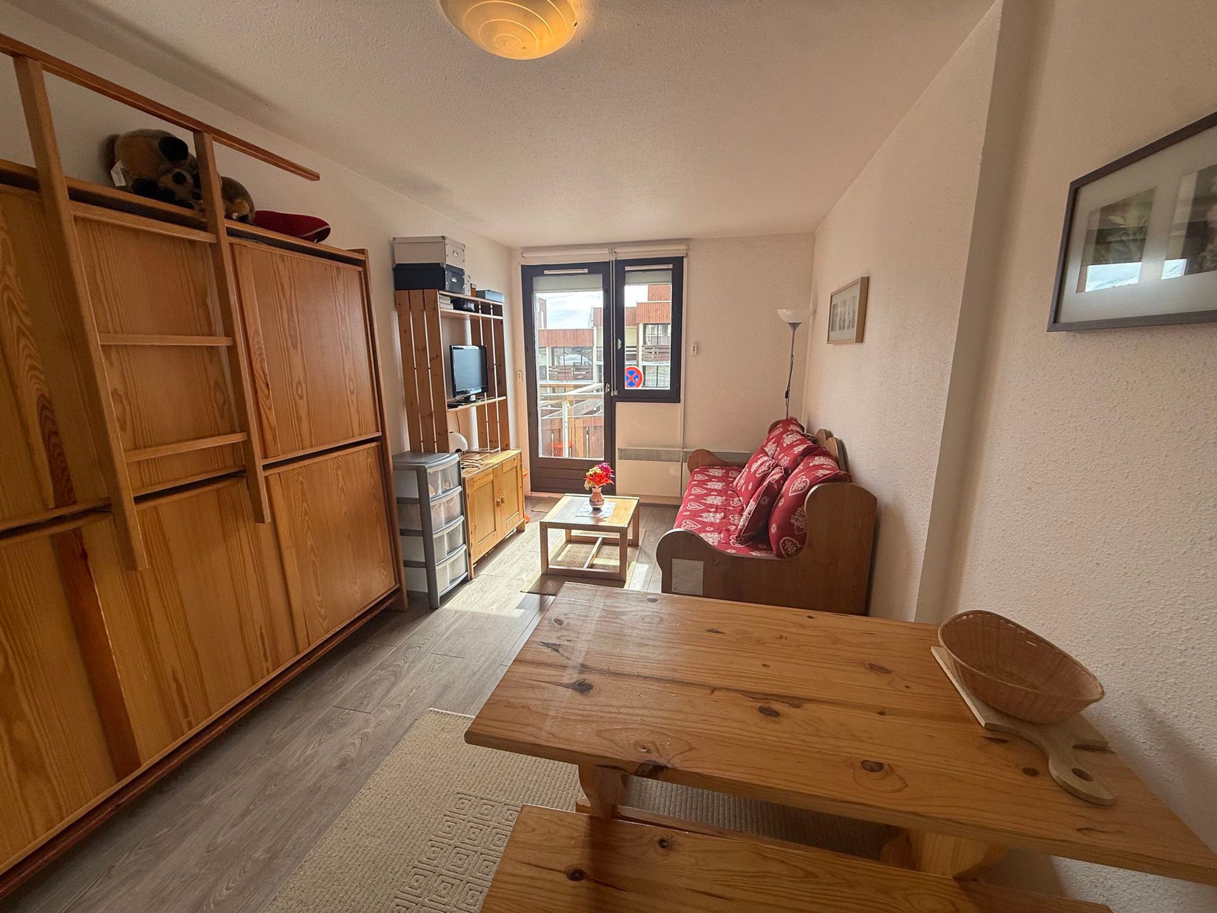 A compact living space with a wooden cabinet, a television on a shelf, a red patterned sofa, and a wooden table.