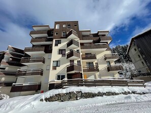 Um edifício residencial com vários andares, varandas, um muro de pedra e neve no chão.