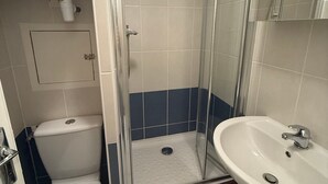 Une salle de bain avec une douche à parois de verre, des toilettes blanches et un lavabo blanc doté d’un robinet chromé.