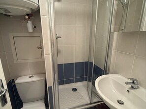 A bathroom with a glass-enclosed shower, a white toilet, and a white sink with a chrome faucet.