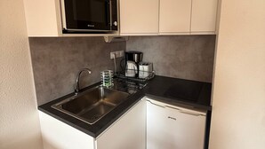 Une petite cuisine équipée d’un four à micro-ondes encastré, d’un évier et d’un réfrigérateur compact.