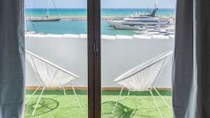 Een balkon met uitzicht op een jachthaven, twee witte stoelen en een heldere lucht.