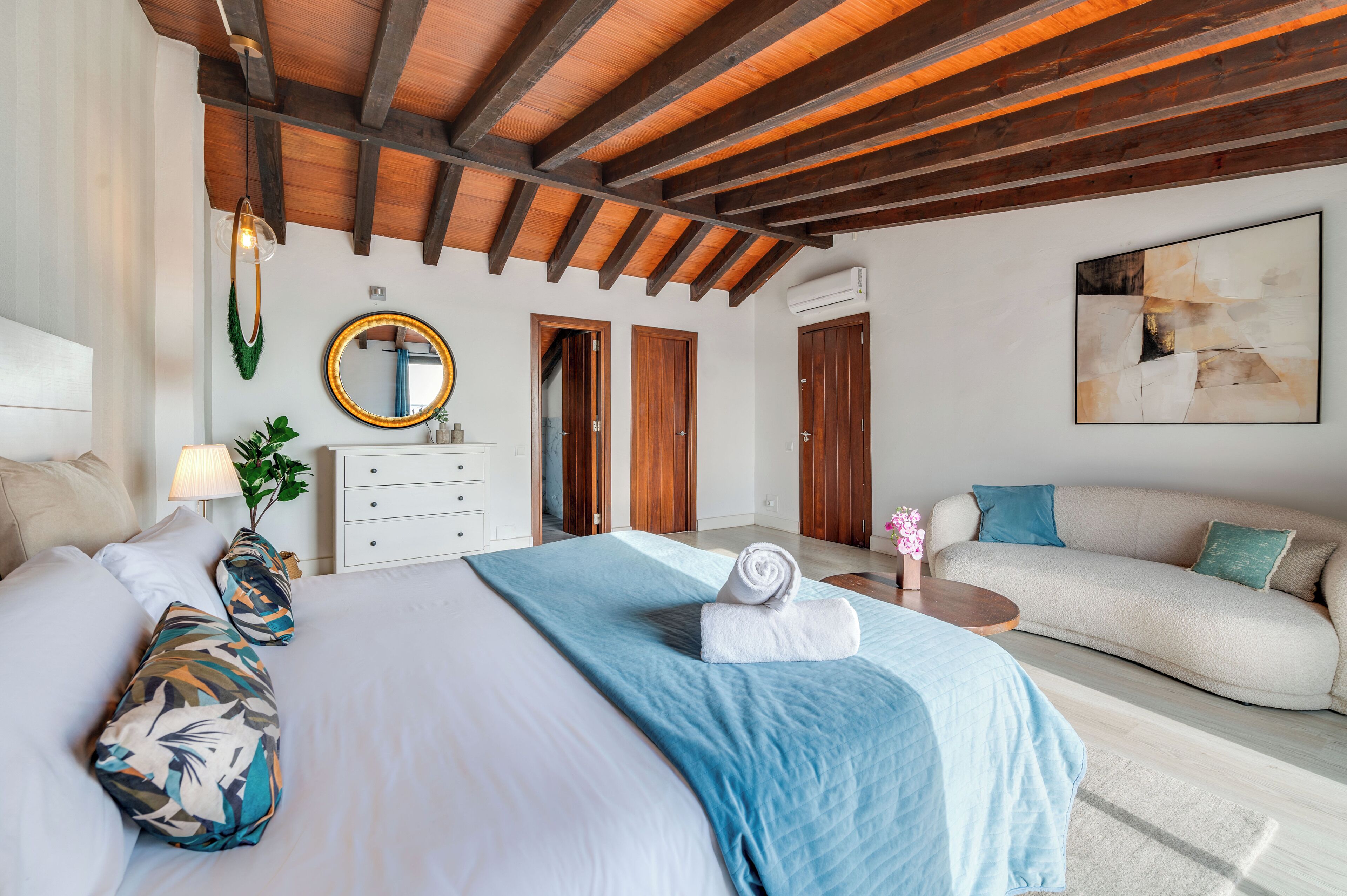 Une chambre d’hôtel avec un lit, un canapé, un miroir rond et des portes en bois.