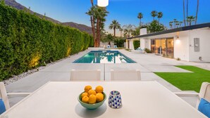 Area piscina moderna all'aperto con tavolo e sedie, una ciotola di limoni e un vaso decorato.