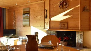 A wooden interior with a fireplace, a dining table set for two, and a television in the corner.