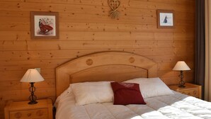 A wooden-paneled bedroom with a large bed, two bedside lamps, and two framed pictures on the wall.