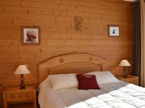 Quarto com painéis de madeira, uma cama grande, duas luminárias de cabeceira e duas fotos emolduradas na parede.