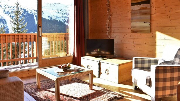 A cozy room with a wooden interior, a television, a sofa, and a dining table with a fruit bowl.
