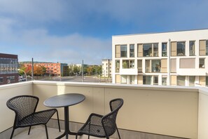 A balcony with two chairs and a table, overlooking a cityscape with modern buildings and a clear sky. - Limehome Potsdam Annemarie-Wolff Platz (Potsdam)