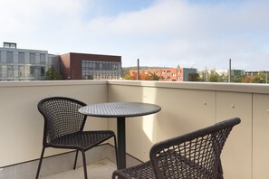 A balcony with two wicker chairs and a round table, overlooking a cityscape with modern buildings. - Limehome Potsdam Annemarie-Wolff Platz (Potsdam)