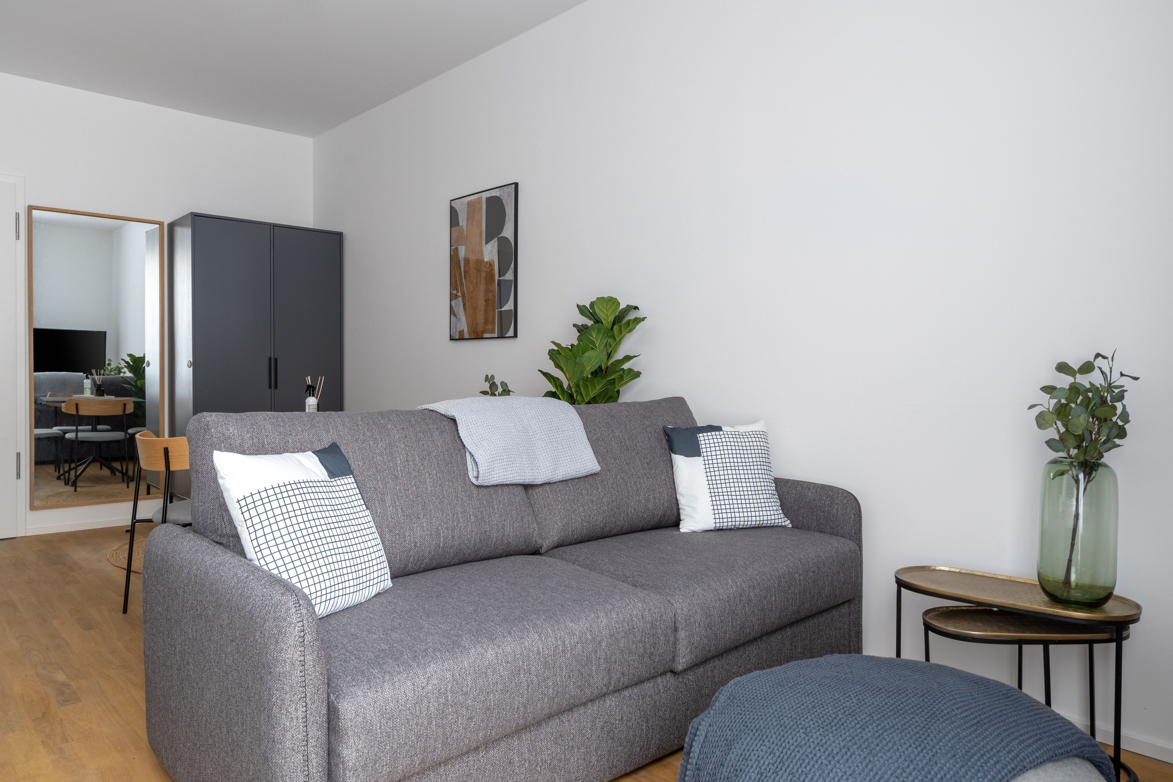 A modern living room with a grey sofa, two pillows, a small side table, and a mirror.