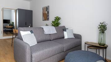 A modern living room with a grey sofa, two pillows, a small side table, and a mirror.