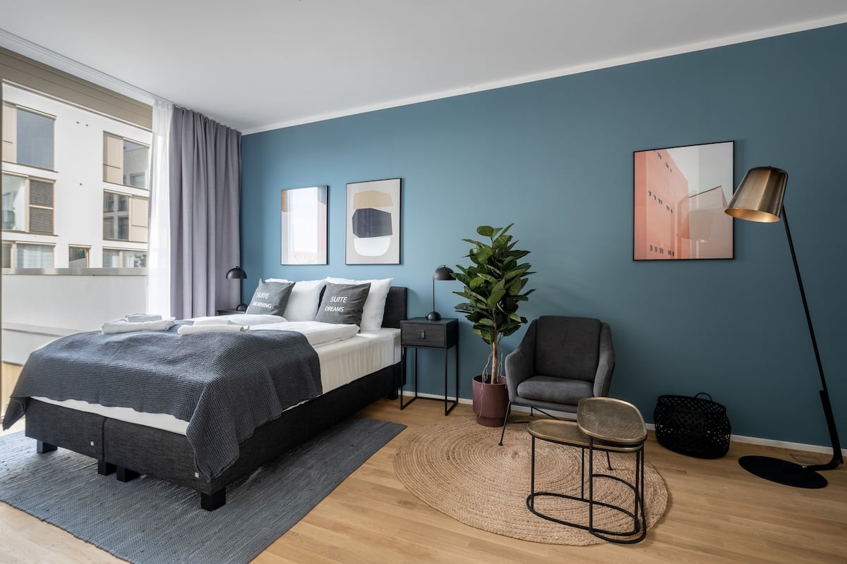 Un dormitorio moderno con cama, mesitas de noche, una silla, una lámpara de pie y una planta en maceta.