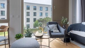 Un apartamento moderno con un ventanal grande, un sofá gris, una mesita redonda y una cama.