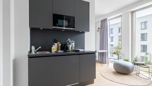 Una cocina moderna con microondas y estufa integrados, un pequeño comedor con una mesa redonda y sillas, y un amplio ventanal con vistas a la ciudad.