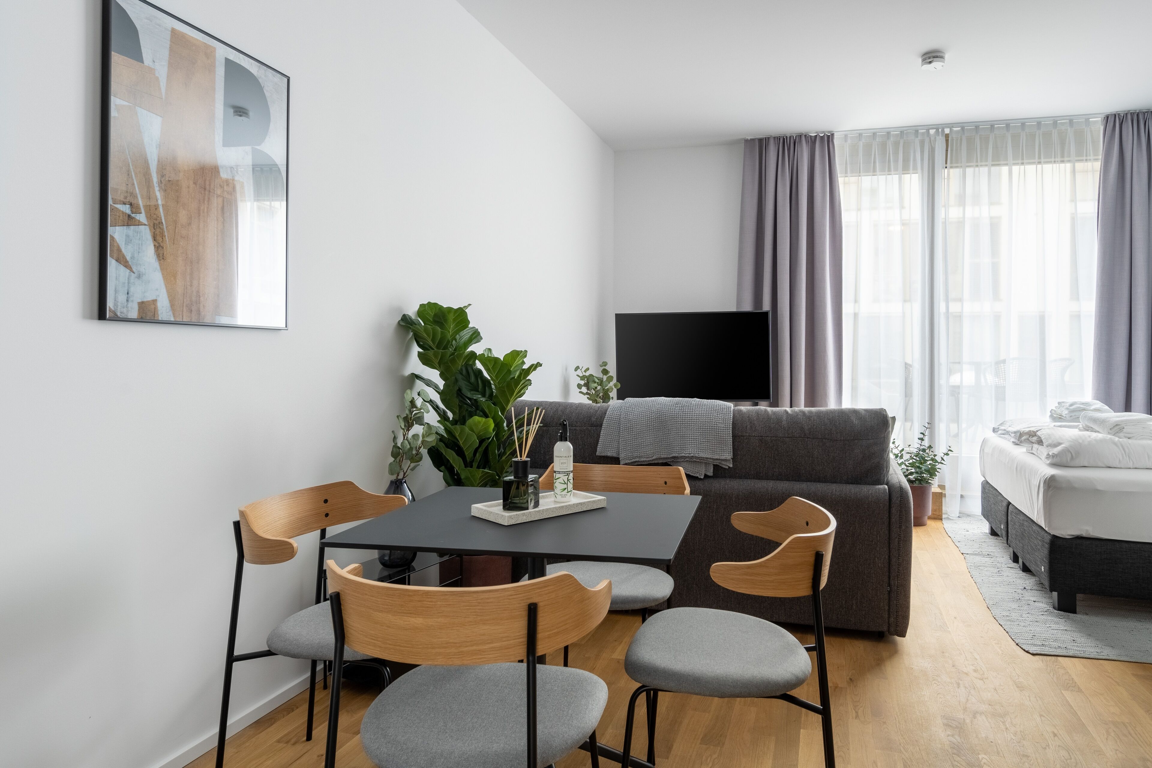 A modern living room with a dining table, chairs, a sofa, a TV, and a bed.