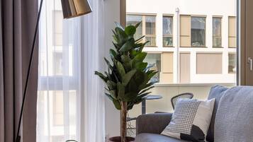 Ett modernt vardagsrum med en grå soffa, ett litet bord, en golvlampa och en krukväxt.