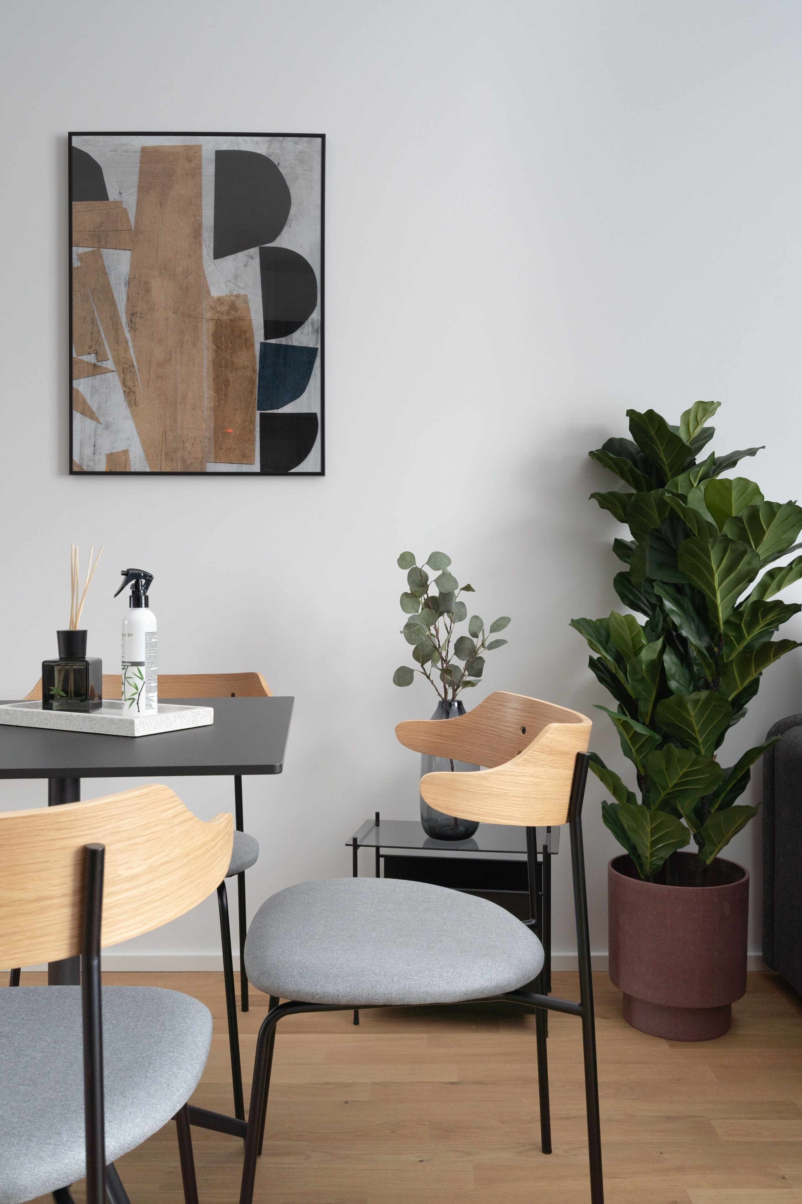 Un comedor moderno con una mesa, sillas, una planta en maceta y una obra de arte abstracto enmarcada en la pared.