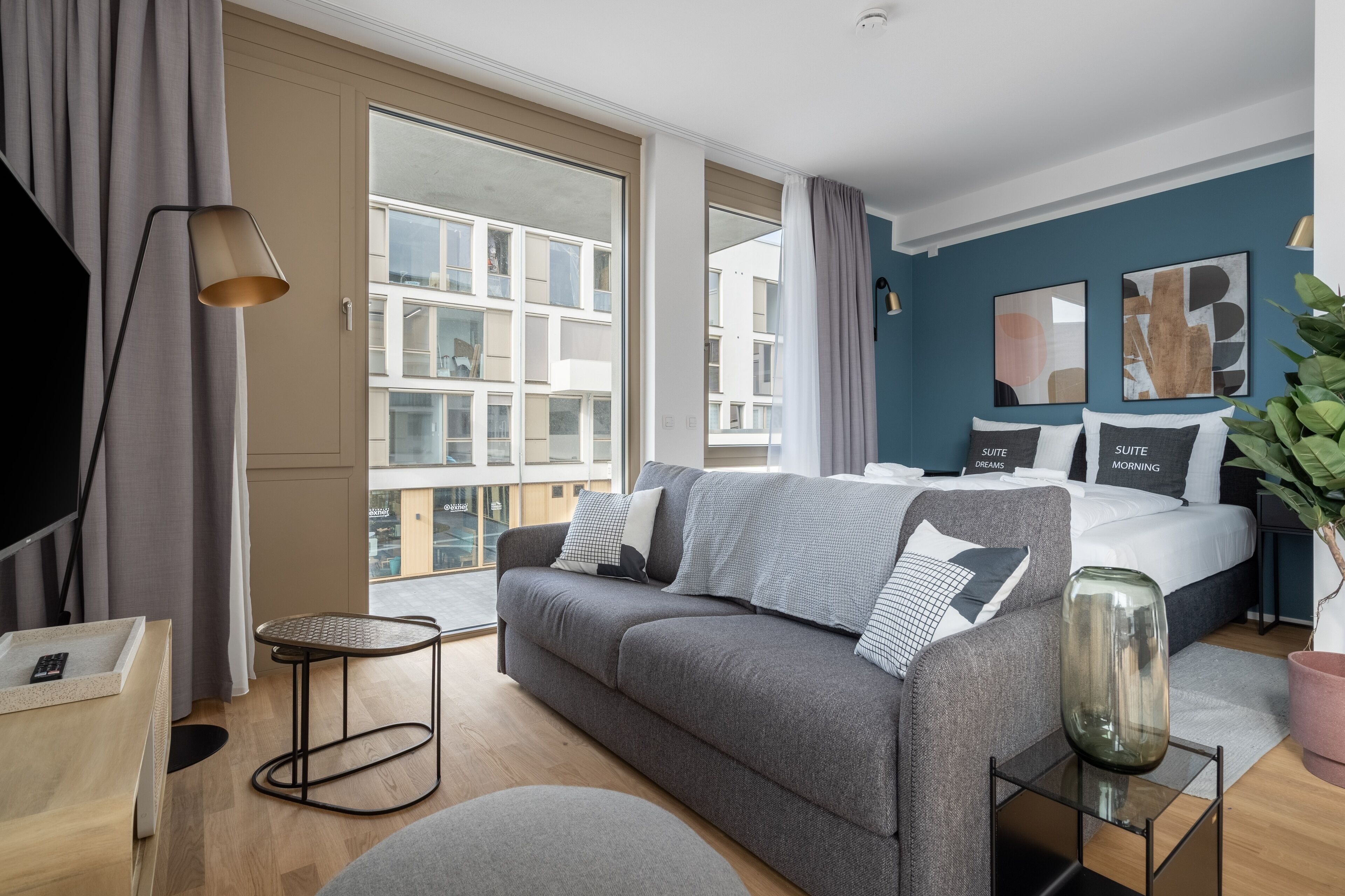 Ein modernes Hotelzimmer mit einem großen Bett, einem grauen Sofa und einem kleinen Tisch.