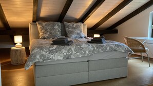 Un dormitorio con cama, lámparas de noche, una silla y una ventana.