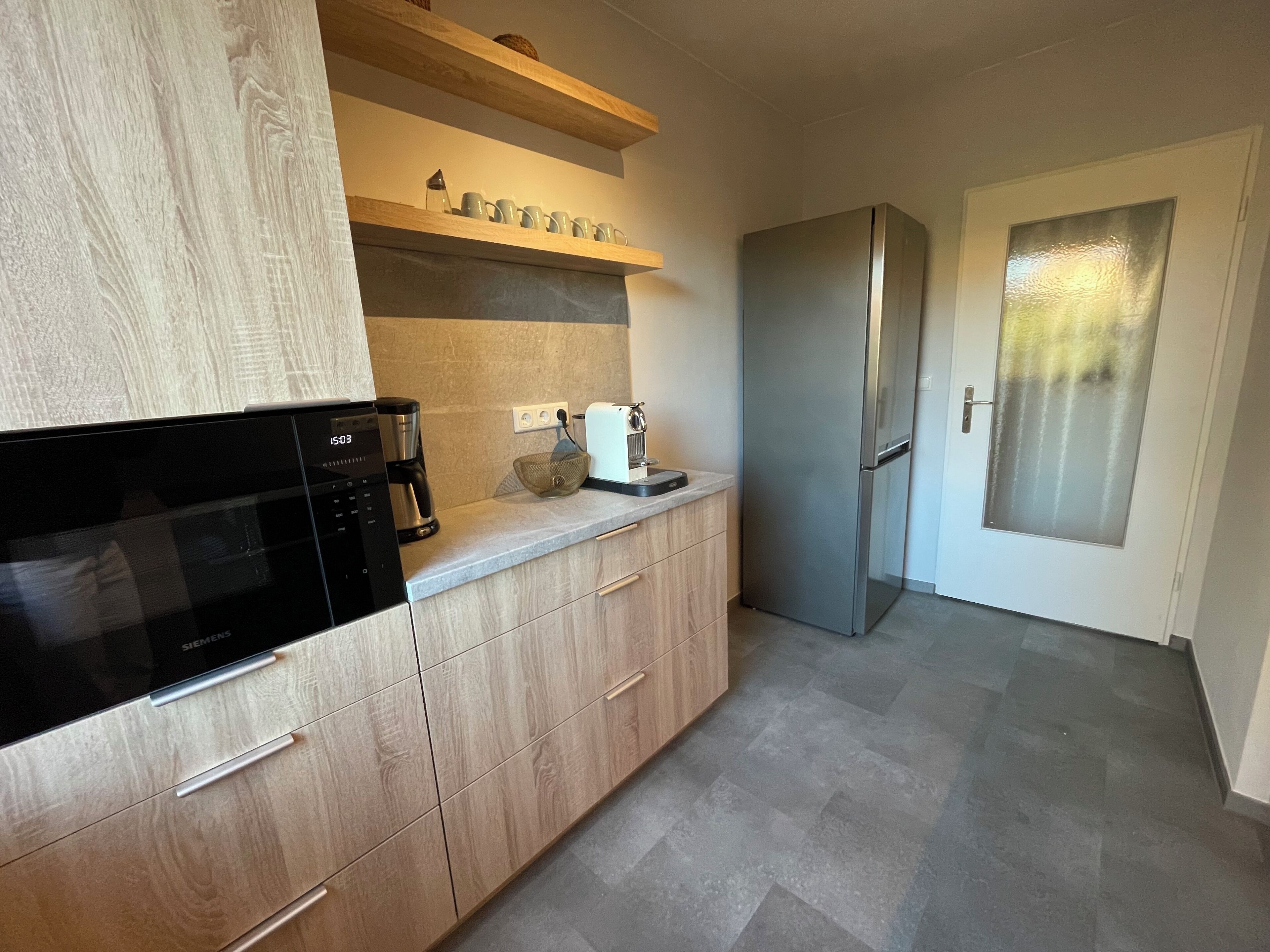 Una cocina moderna con armarios de madera, un refrigerador de acero inoxidable, una cafetera y un microondas.