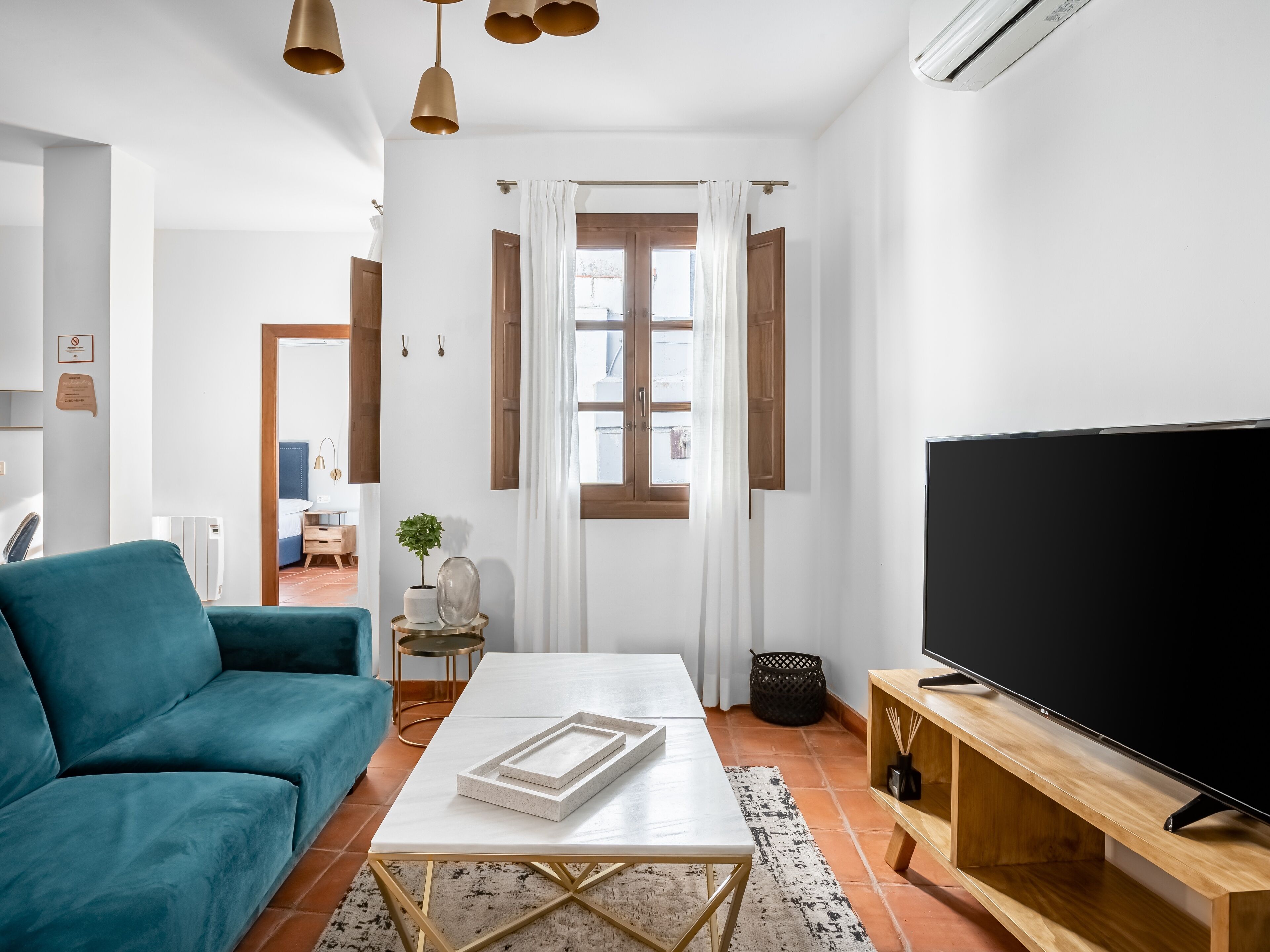 Un salon moderne avec un canapé de couleur turquoise, une table basse blanche et un grand téléviseur à écran plat posé sur un meuble en bois.