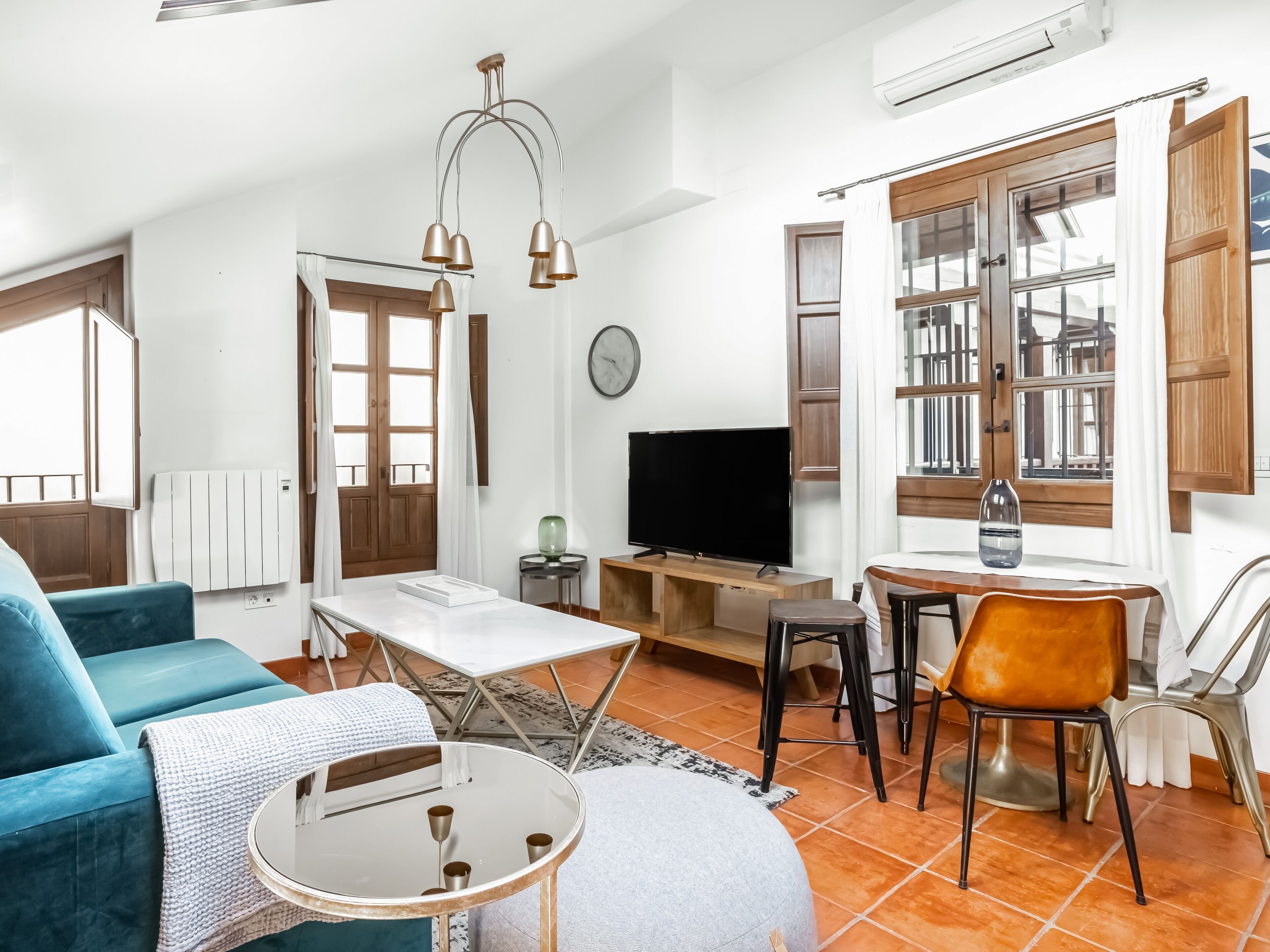 Una sala de estar moderna con un sofá azul, una mesa de centro redonda, un televisor y una zona de comedor con una mesa y sillas.